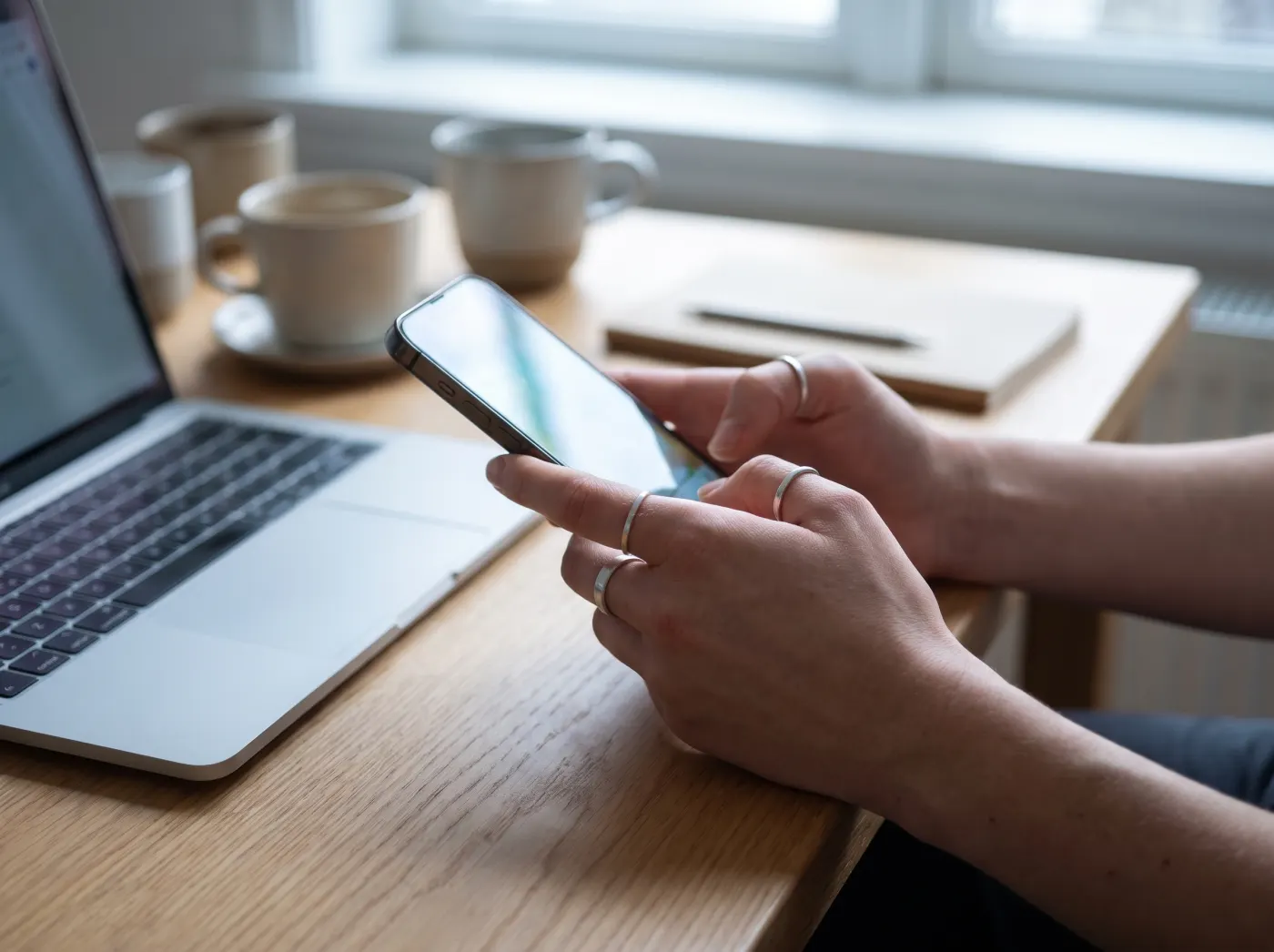 Hands holding a smartphone next to a laptop